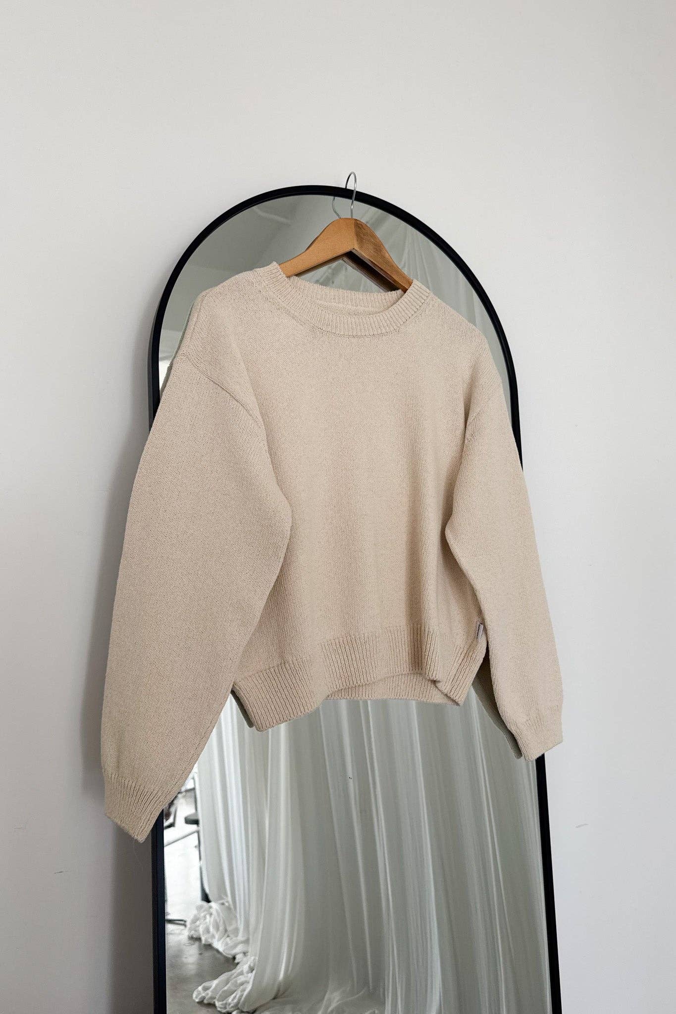 Cream Le Bon Shoppe sweater on a hanger in front of a mirror