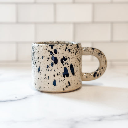 Speckled ceramic mug on a marble surface with a tiled wall background