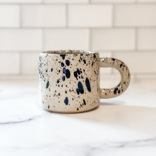 Speckled ceramic mug on a marble surface with a tiled wall background